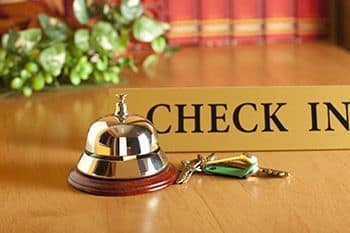 A hand reaching for a concierge desk bell in a luxurious hotel lobby.